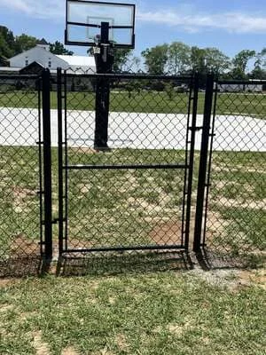Black chain link fence with gate and basketball hoop in residential yard
