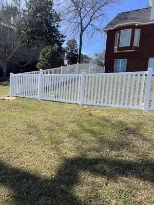 White vinyl picket fence installed along residential property with brick home in background