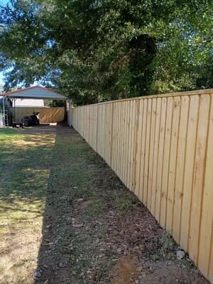 Tan corrugated metal privacy fence with mature trees