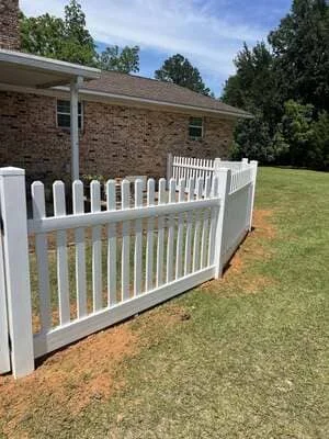 White vinyl picket fence installed along brick home with manicured lawn